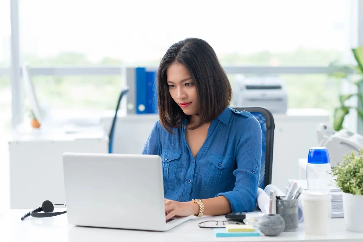 A woman sitting at her desk on top of the laptop.