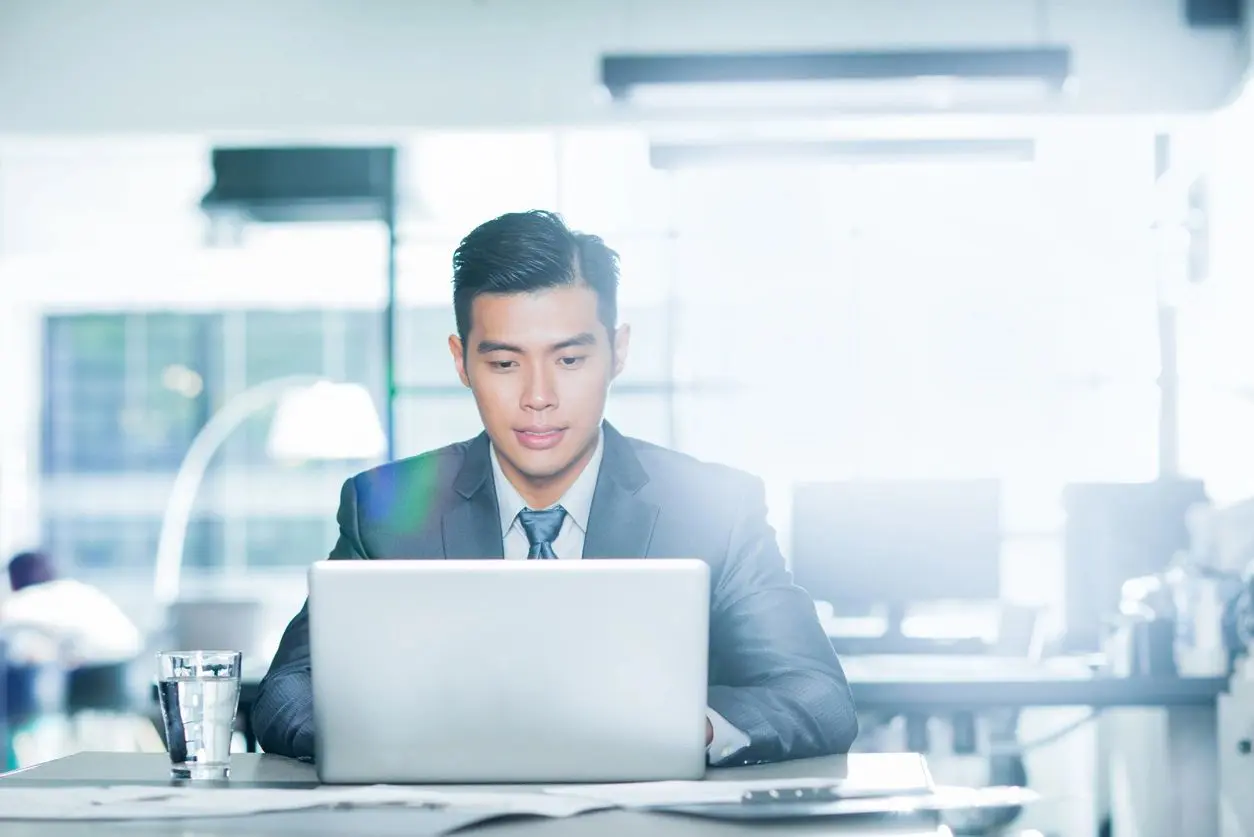 A man in suit and tie sitting at a table with a laptop.