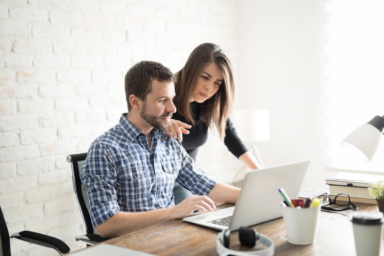 A man and woman sitting at a table looking at a laptop.