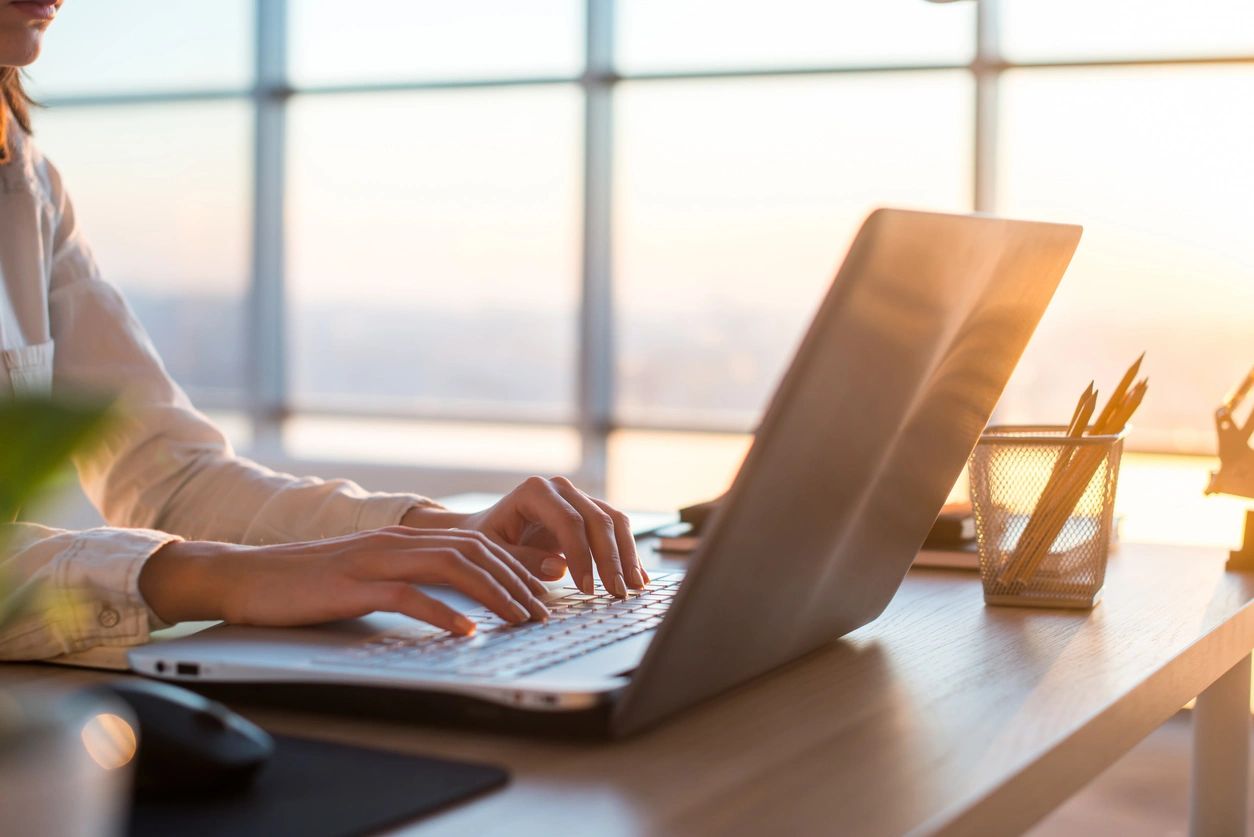 A person typing on a laptop in front of a window.